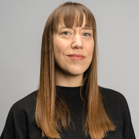 A studio portrait of a white woman with long straight light brown hair wearing a black top.